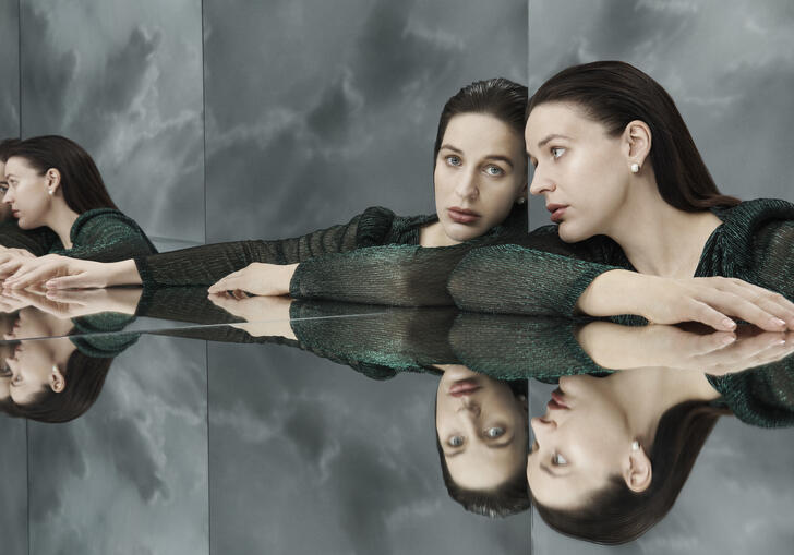 A brunette woman stars at her own reflection, repeated multiple times