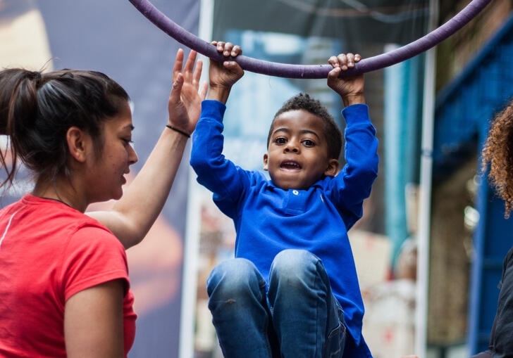 A child hanging from an aerial hoop with support from two workshop facilitators