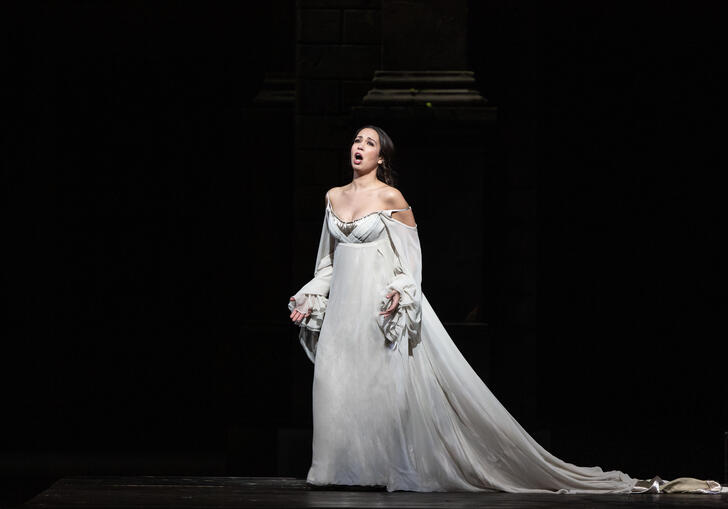 A woman in a white dress sings on a stage.