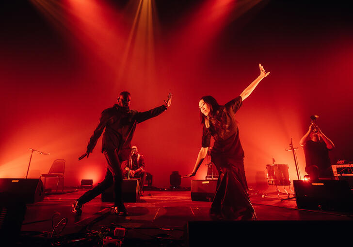 Hand to earth performing on stage with Daniel Wilfred and Sunny Kim in the foreground bathed in a red light 