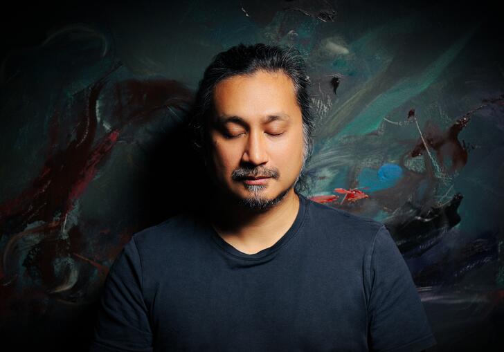 Headshot of an Asian man against a dim colourful background