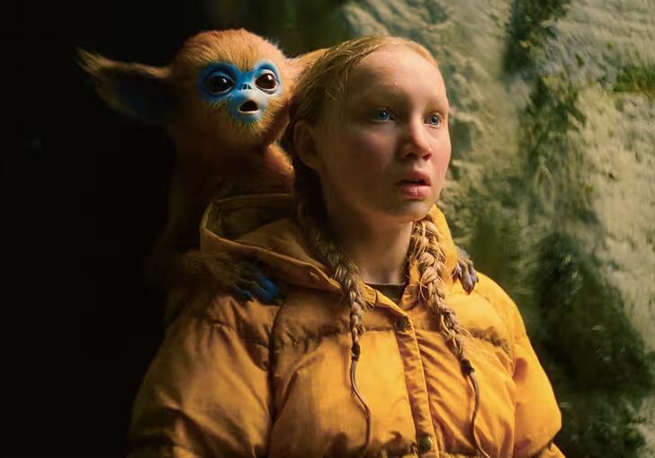 A young girl wearing a yellow puffer coat has a fantastical creature on her shoulder