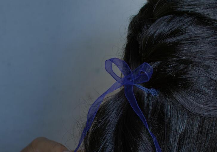 Close up of the back of head of a girl or woman with dark hair, tied with a blue bow