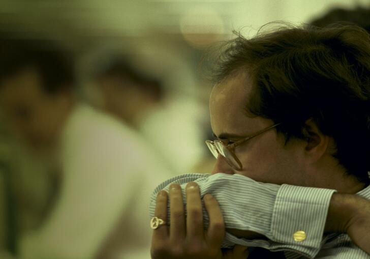 Man in smart clothing in glasses and with gold ring looks worried, covering his mouth with his arm