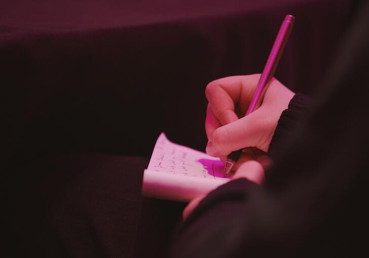 A person's hand holding a small notepad as they write in it