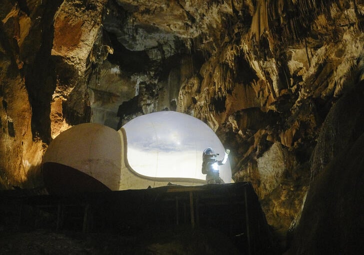a person in a spacesuit in a cave near a spaceship