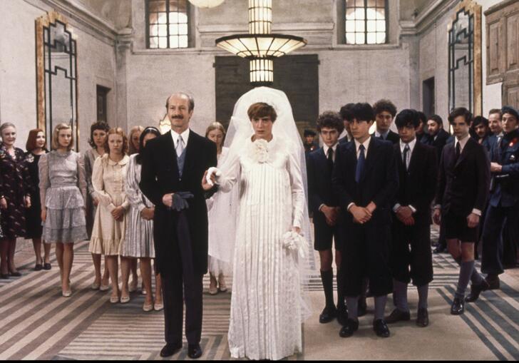 A man and a woman dressed in wedding attire with people standing behind them.