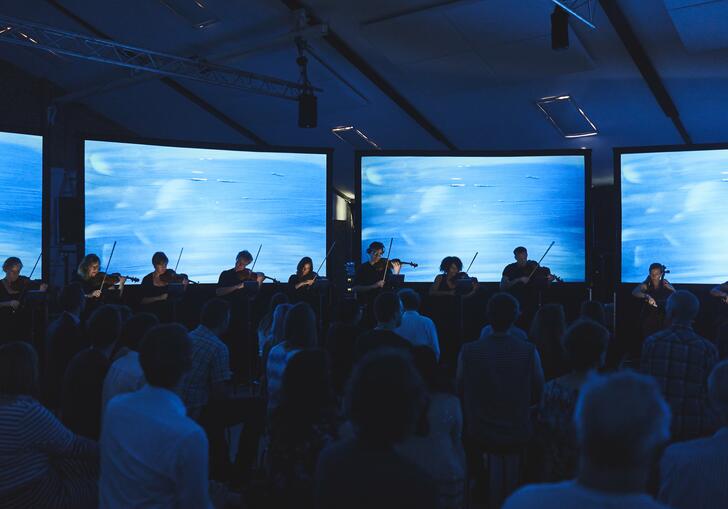 A small quartet performing in front of an audience with four screens behind them