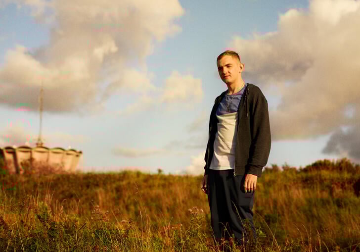 A young white man stands in a field looking into the sunset