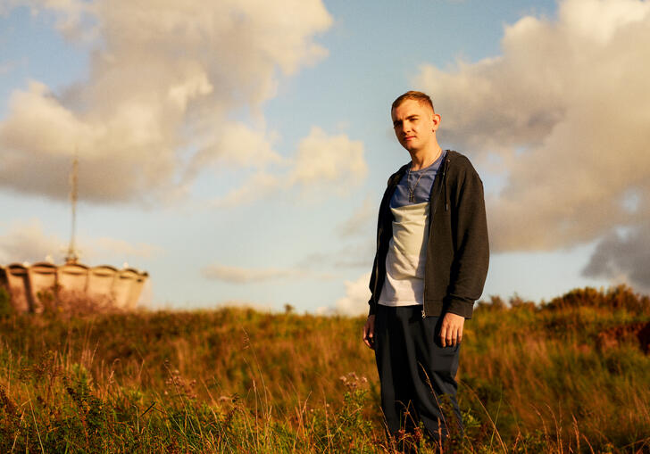 A man stands in a field looking towards the sunset