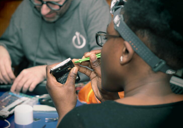 A repairer fixing a small device across from another volunteer with Restart London.