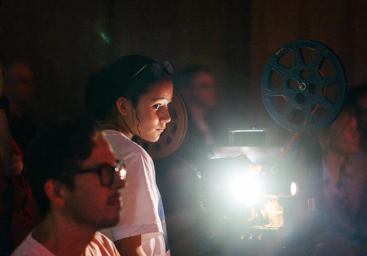 A group of people and a young child look on. A film projector emits light