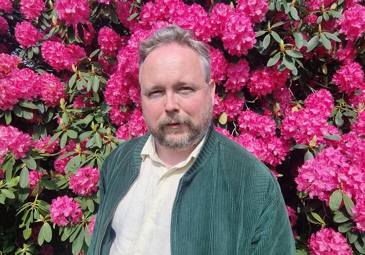 Richard Dawson stood in front of a wall of flowers