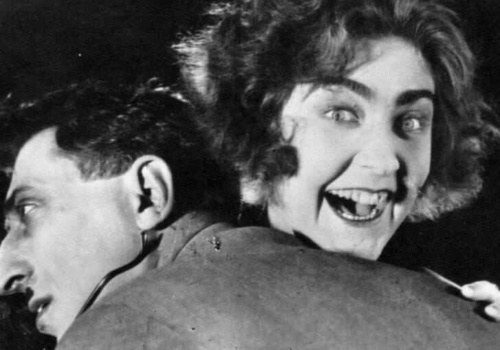 A woman hugs her husband with a deranged look in her eyes