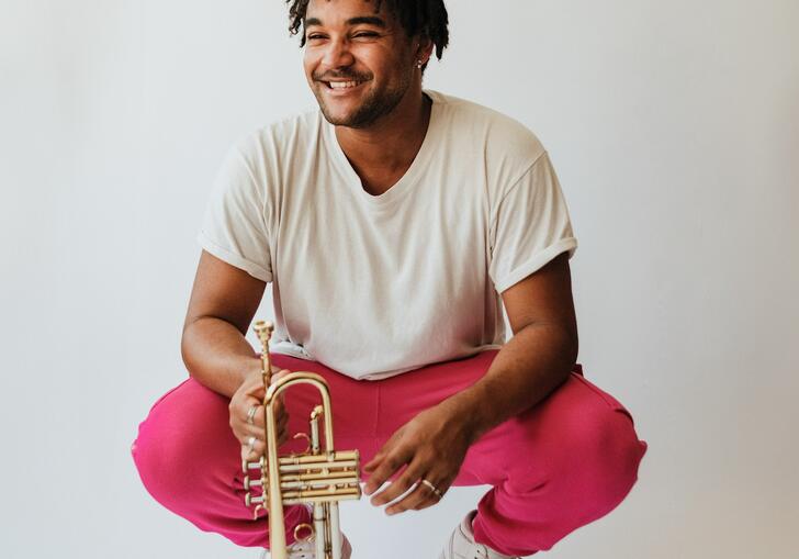 Aaron Akugbo crouching while holding a trumpet