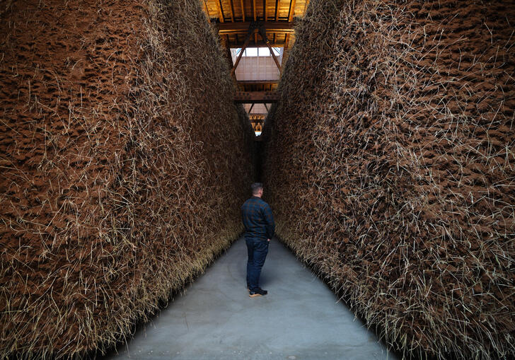 A man stands in between two walls of mud in an art installation. 