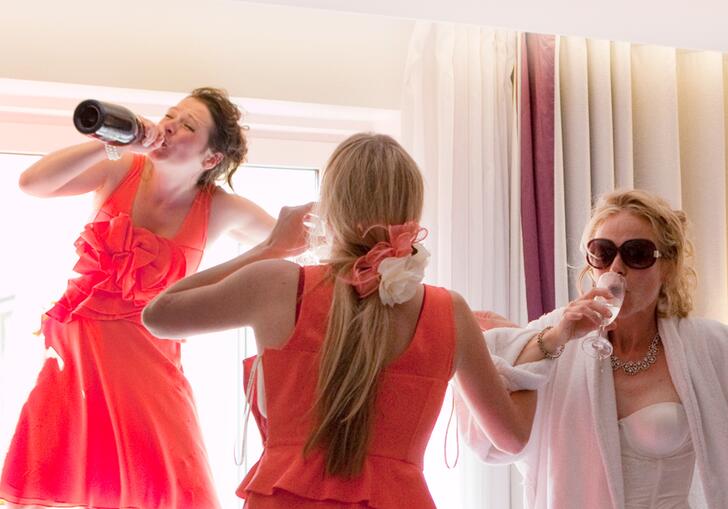 A bride and her two bridesmaids down prosecco in a hotel room.