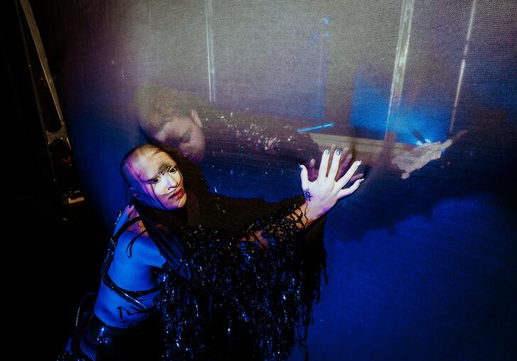 A person with a black veil over their arms presseing against a thin partiton while another person does the same on the other side