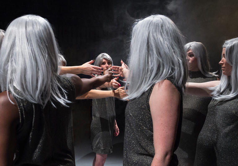 Photos which shows a group of women with identical silver wigs holding their hands out into a circle