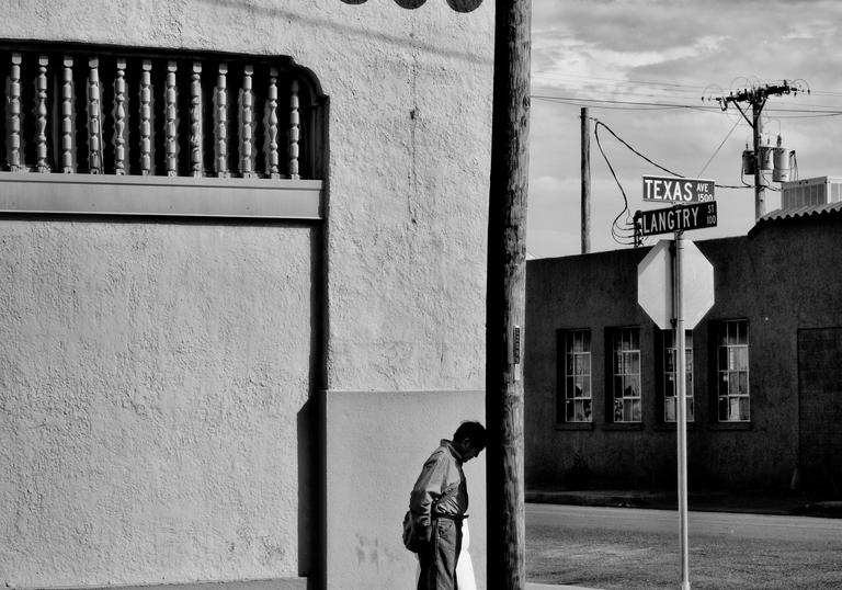 Photo of figure standing on a street corner by a lamppost