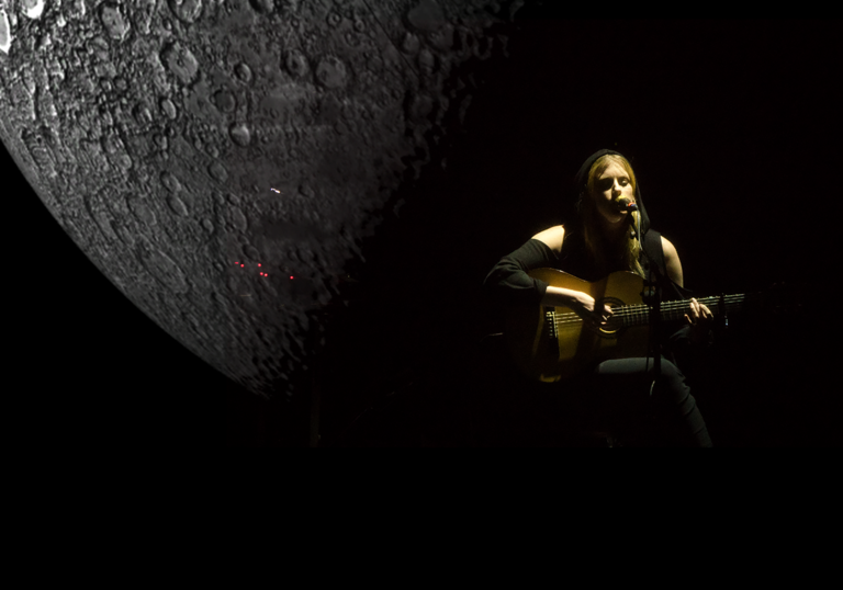 Susanne playing guitar next to a projection of a giant moon