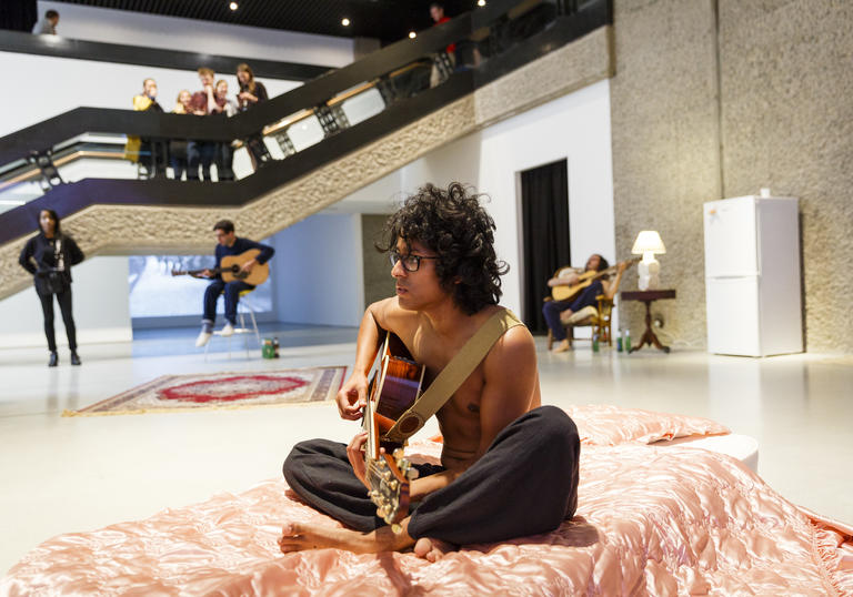 Man sitting on a bed playing guitar