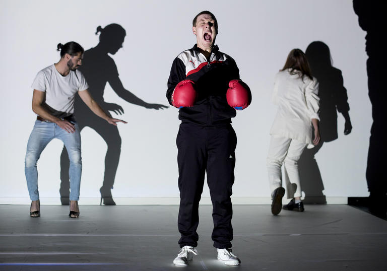 three people on a stage, one wears boxing gloves and screams