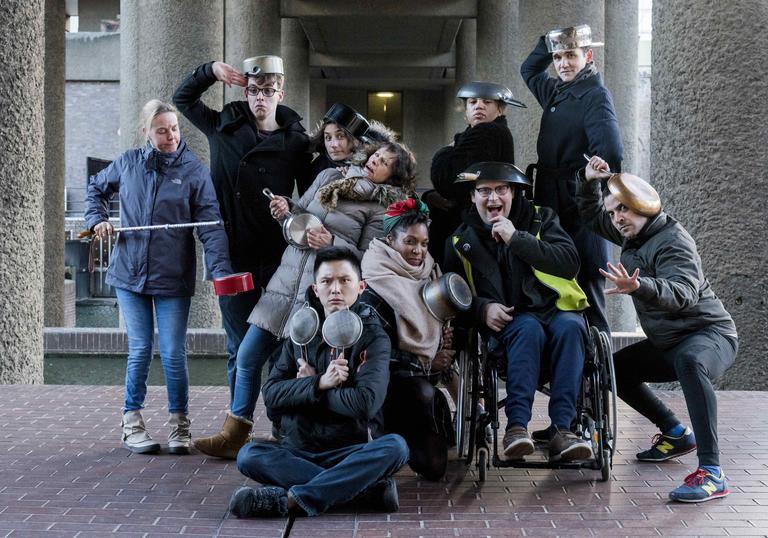 A group photo of the actors from Told By An Idiot standing together doing funny poses with pots and pans on their heads