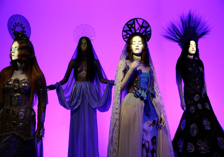 Installation image of Gaultier exhibition with pink background and four mannequins in gowns