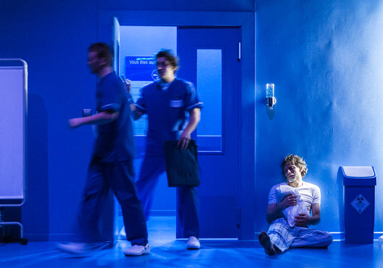 Hospital room with a person sat on the floor and 2 hospital workers going through the door