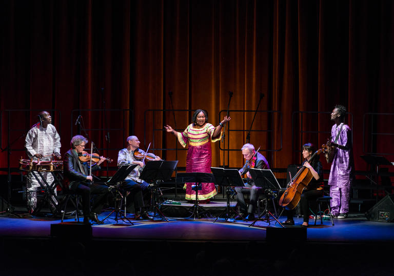 Kronos Quartet performing with Trio Da Kali on a stage with a red curtain backdrop