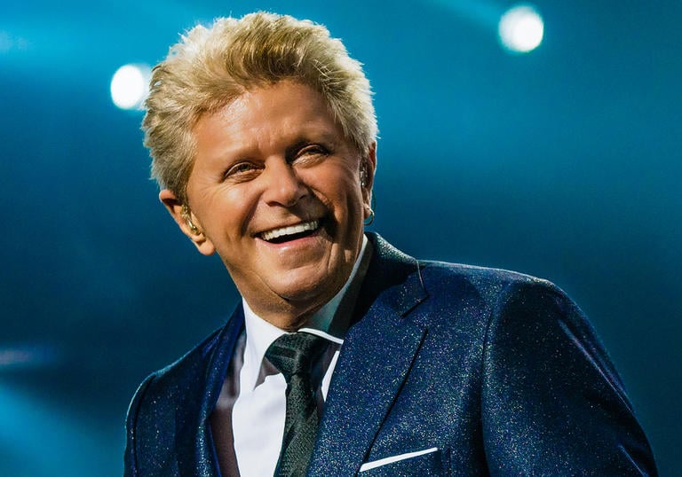 Peter Cetera smiling on stage in a blue sparkly jacket