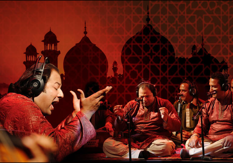 Rizwan-Muazzam Qawwali perform tradition instruments and sing seated with a backdrop of a mosque