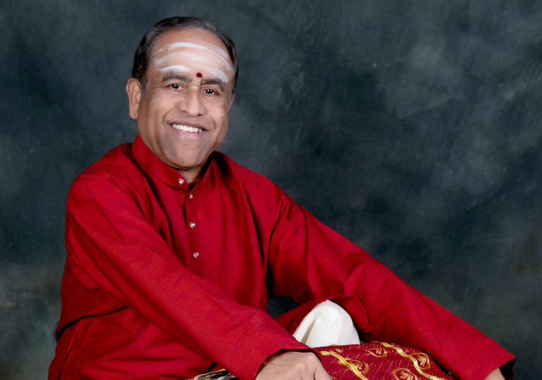 Dr. Trichy Sankaran is holding a drum and smiling
