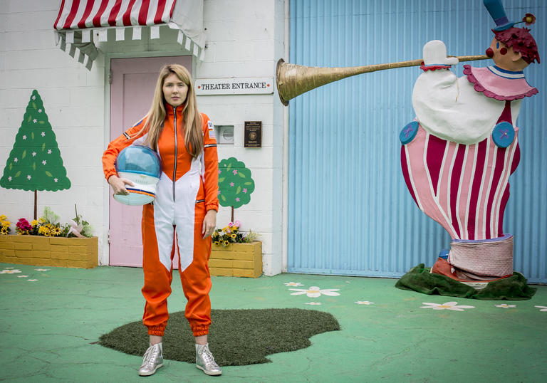 Beatie Wolfe wearing an orange space suit and holding a helmet