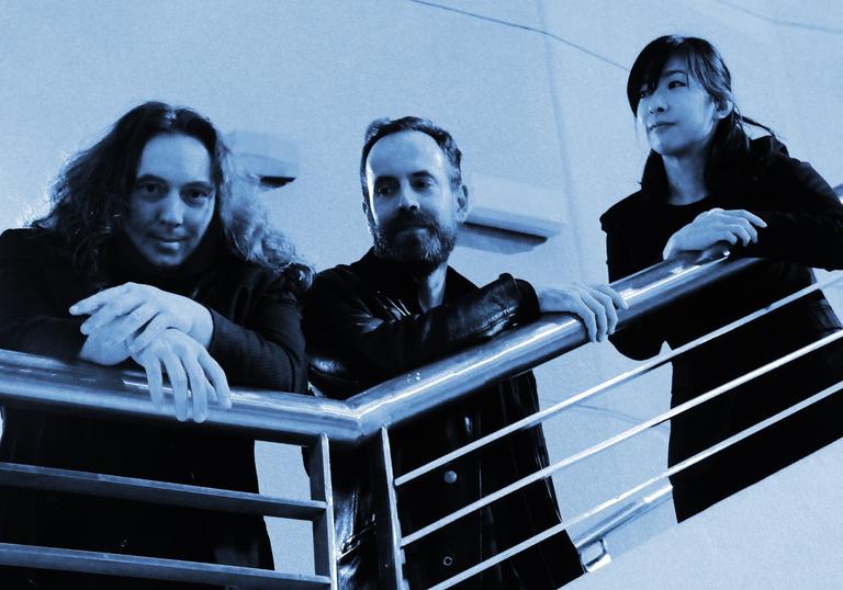 Tangerine Dream are photographed in a dreamy blue filter on what appears to be the upper deck of a small commercial ferry