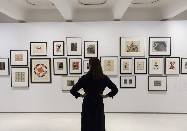 A woman looks at a selection of art, they're from the exhibition Modern Couples. She seems to be enjoying herself, encouraging the viewer to book tickets