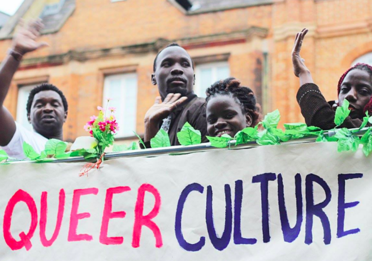 a group of people stand on a stage with a banner saying queer culture on it