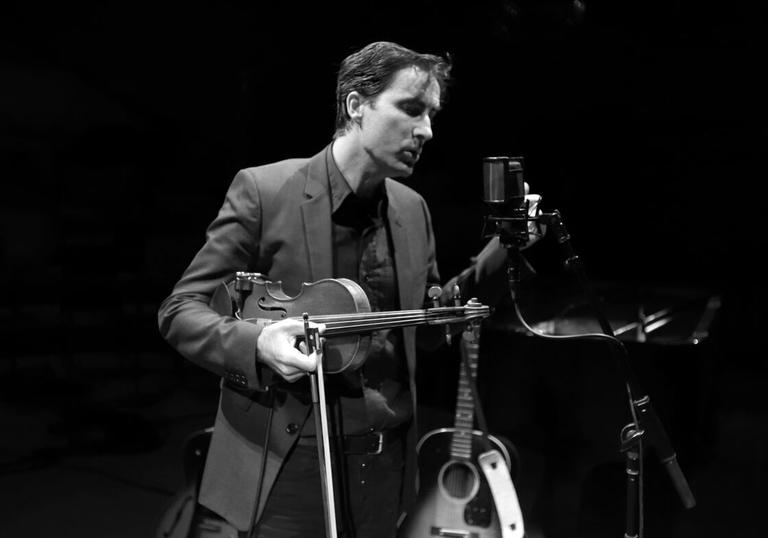 Andrew Bird holding his violin and singing into a microphone