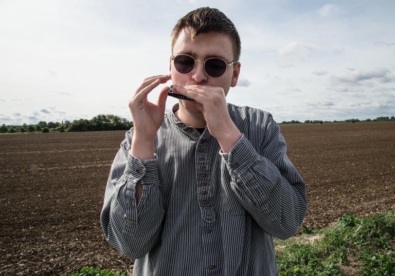 Oliver Cross playing his harmonica in a field
