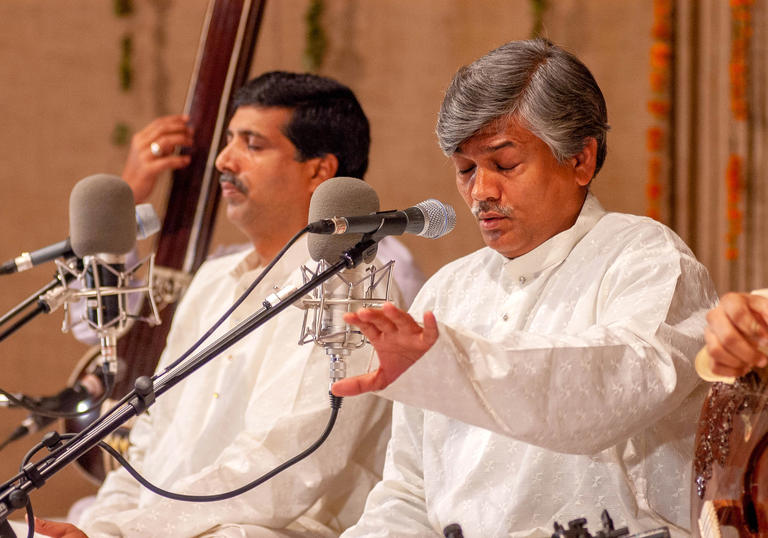 The Gundecha brothers wearing white and singing into microphones