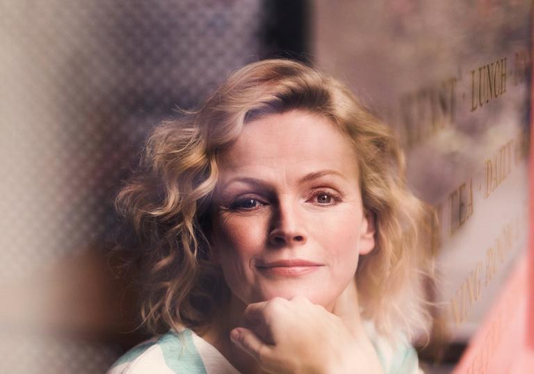 Image of actor in white and green t-shirt gazing out from cafe window