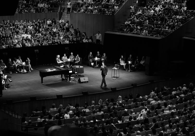 Nick Cave on stage with a microphone, a piano in front of him