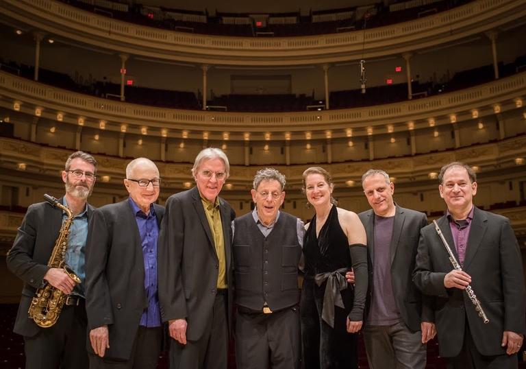The Philip Glass Ensemble with Philip Glass pose for a photo in a concert hall