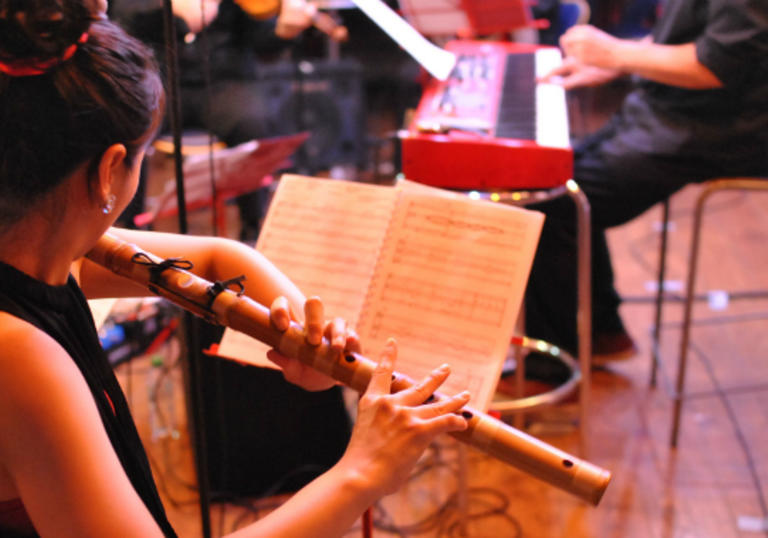 A woman playing flute and reading a piece of music