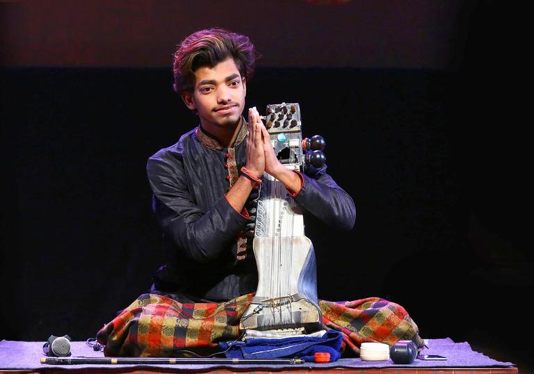 Momin Khan presses his hands together, seated on stage