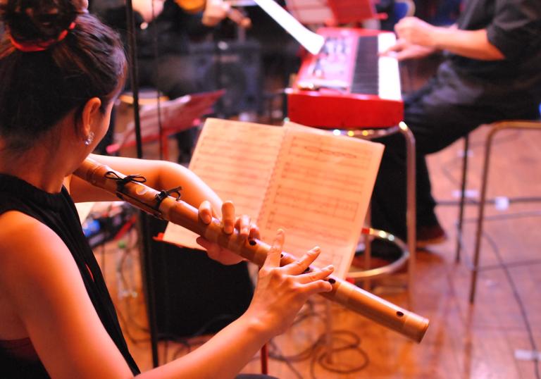 Hyelim Kim plays a wooden flute with other musicians in the background