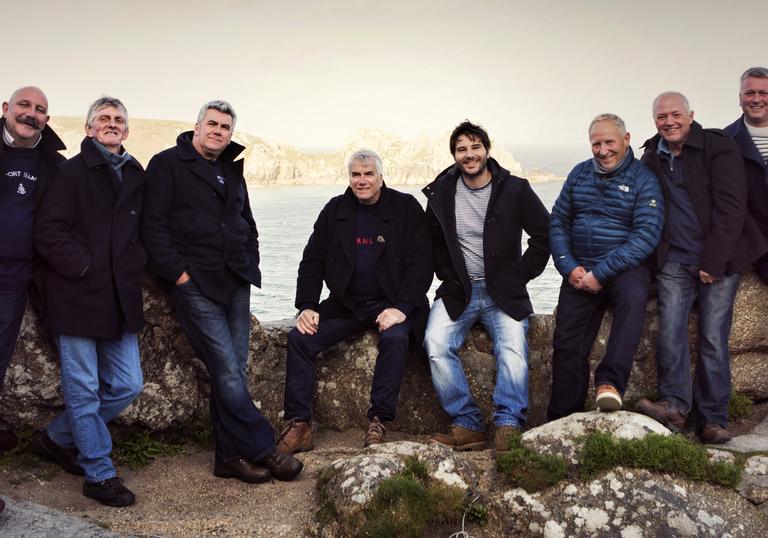 Fisherman's Friends seated on rocks on the Cornish coast