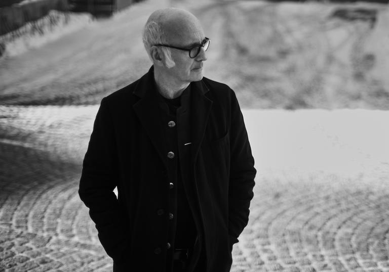 Ludovico Einaudi standing outside with his hands in his pockets, looking to his left.