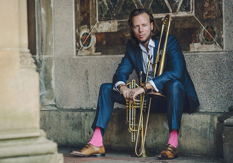 Jazz trombonist Elliot Mason sitting down in blue suit